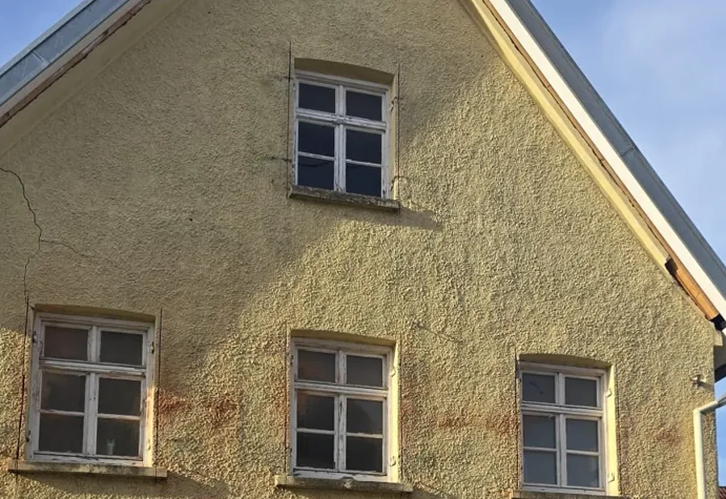 Vorher: Giebelseite eines Altbaus mit alten, verwitterten Holzsprossenfenstern